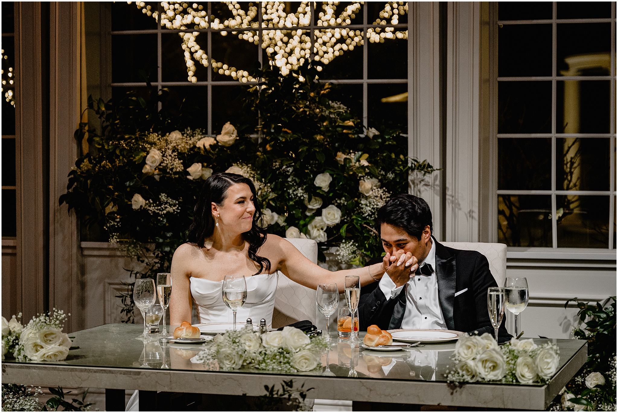 groom kisses bride's hand sitting at sweetheart table at the Estate at Florentine Gardens