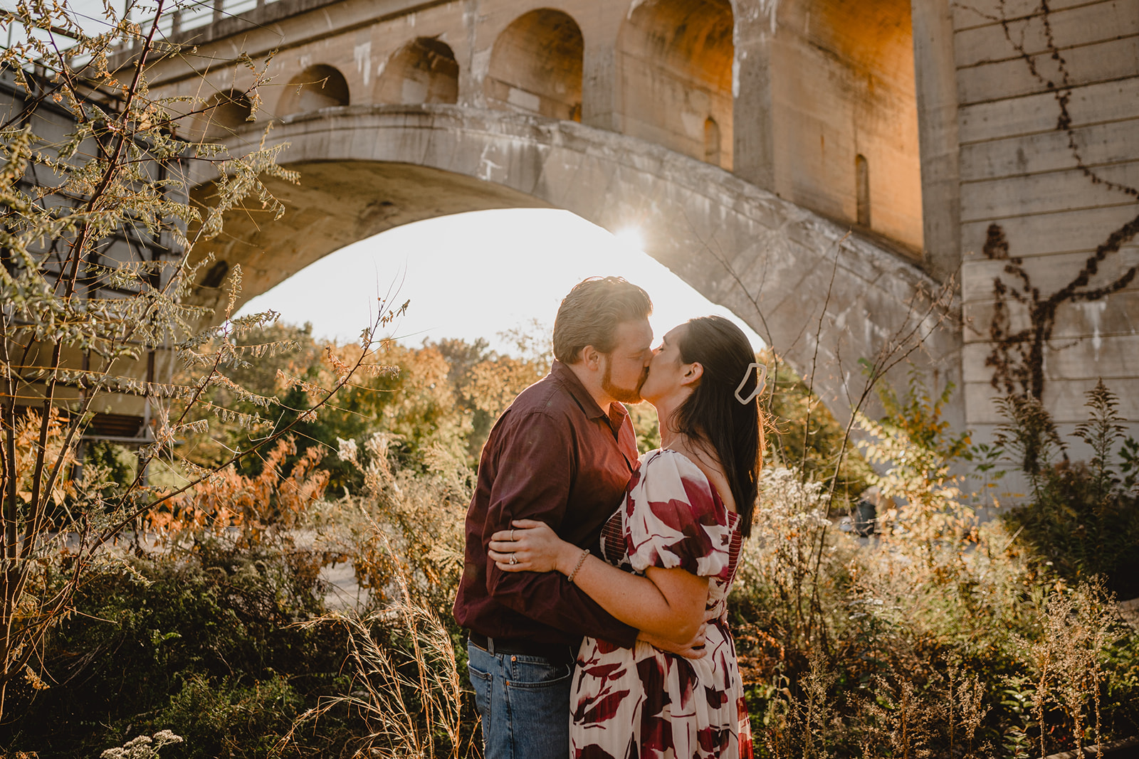 man and woman stand kissing in front of bridge over Schuylkill River