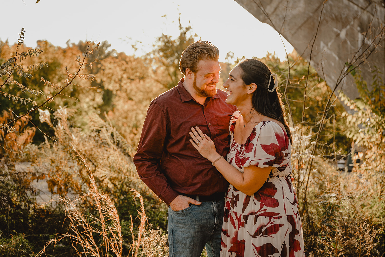couple laughs in front of Schuylkill River during Philly engagement session