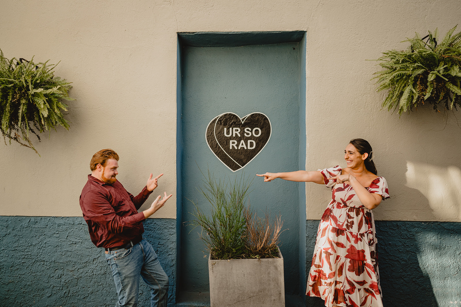 couple points at each other in front f artwork that says UR SO RAD