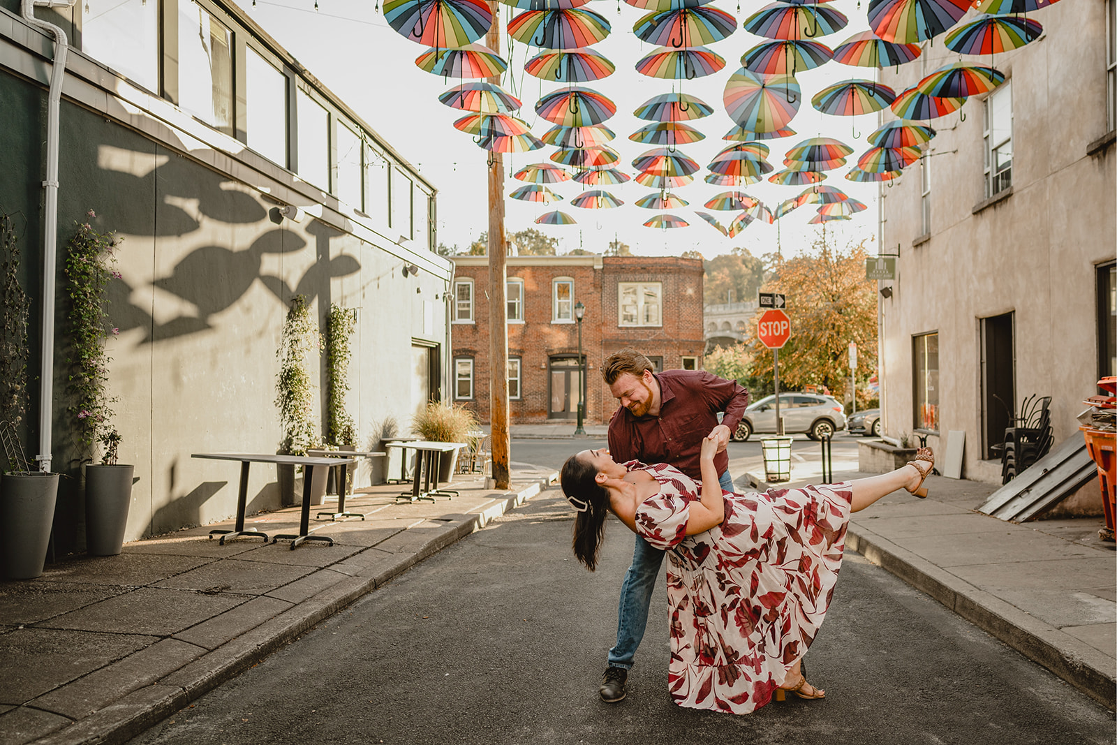 man dips woman under colorful umbrellas hanging between buildings in Manayunk 