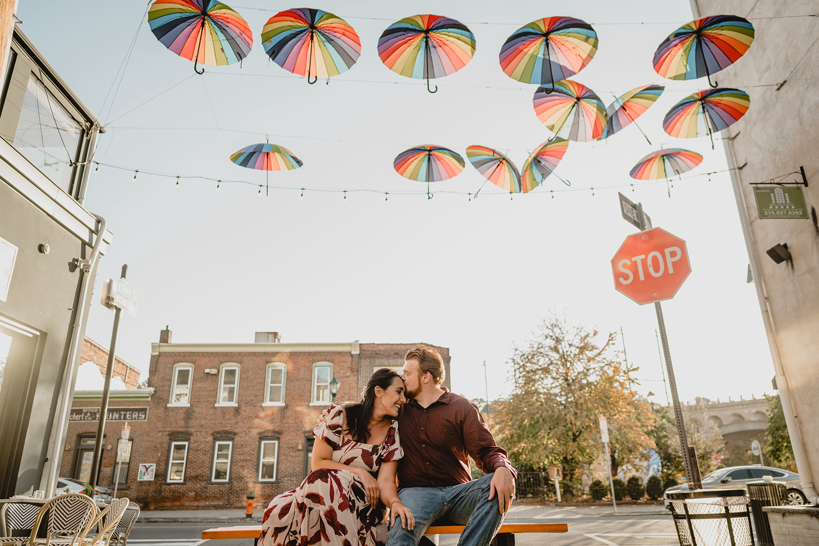 man hugs woman to him kissing her forehead under hanging umbrellas