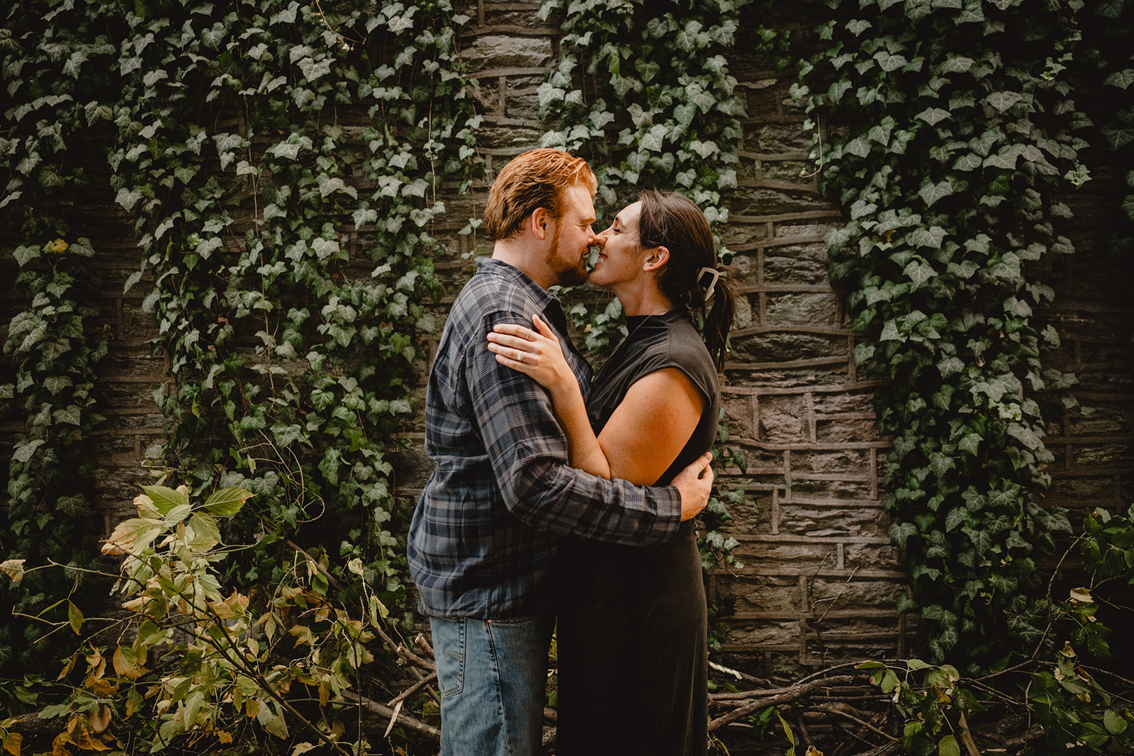 engaged couple kisses in front of ivy covered wall in Manayunk neighborhood