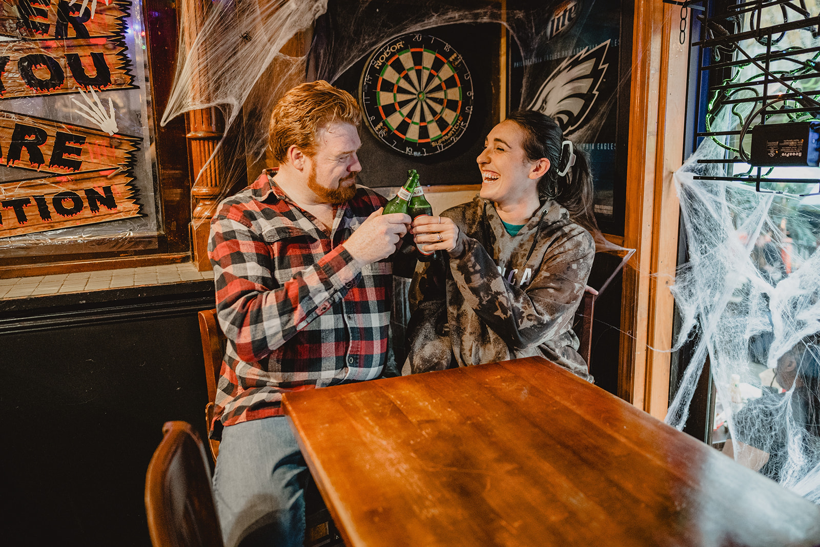 couple toasts beers during engagement photos in Manayunk bar