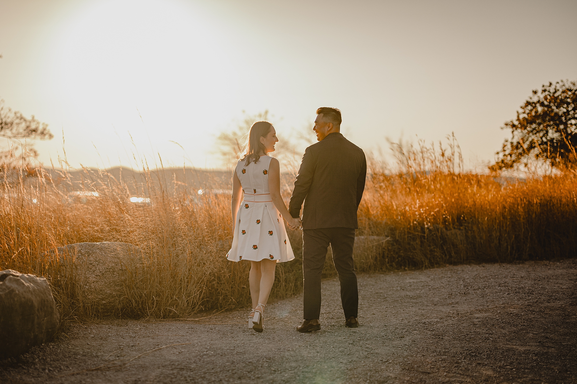 engaged couple holds hands talking at sunset on mountaintop 