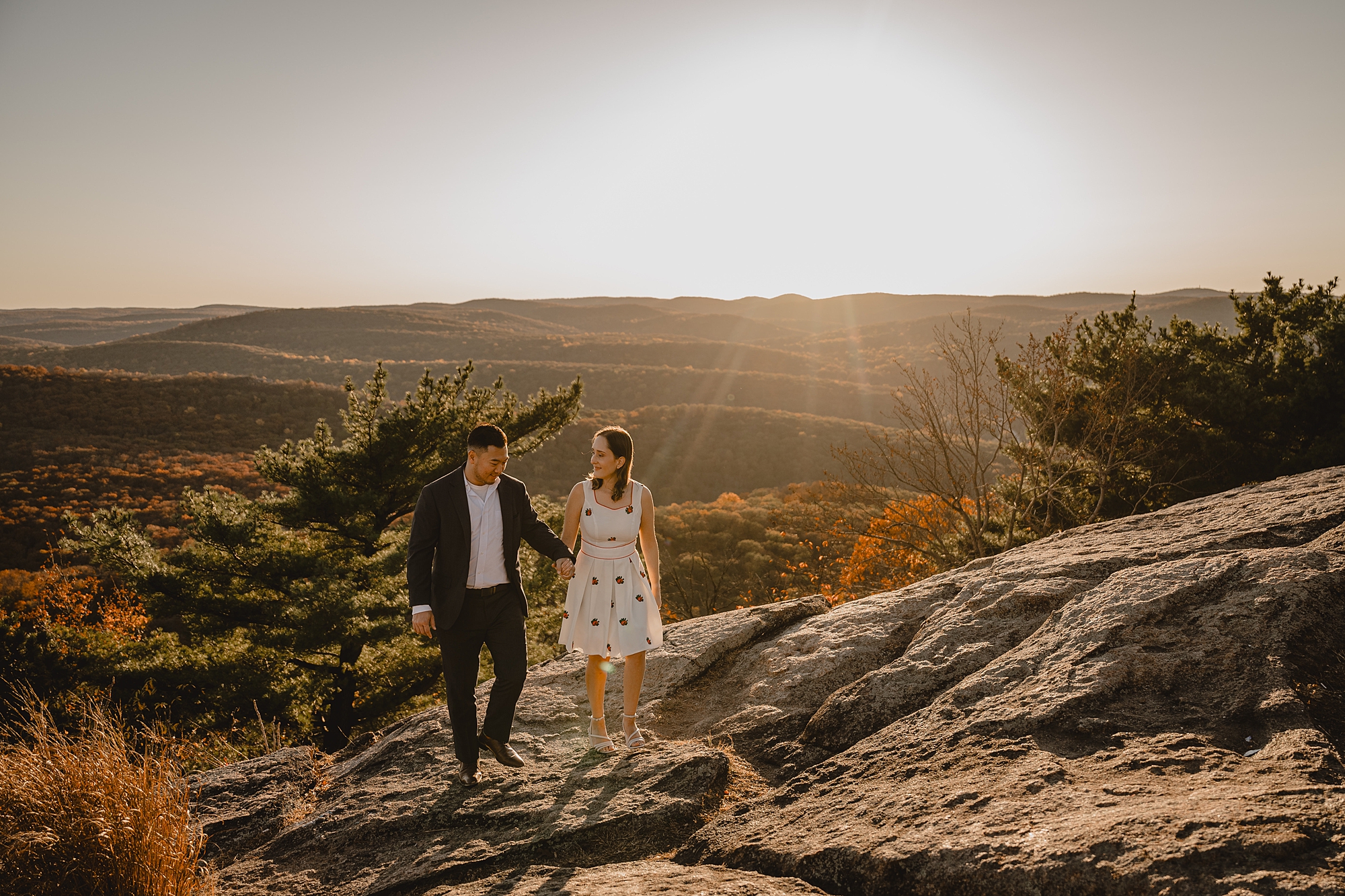 couple walks down mountaintop during fall engagement session on Bear Mountain