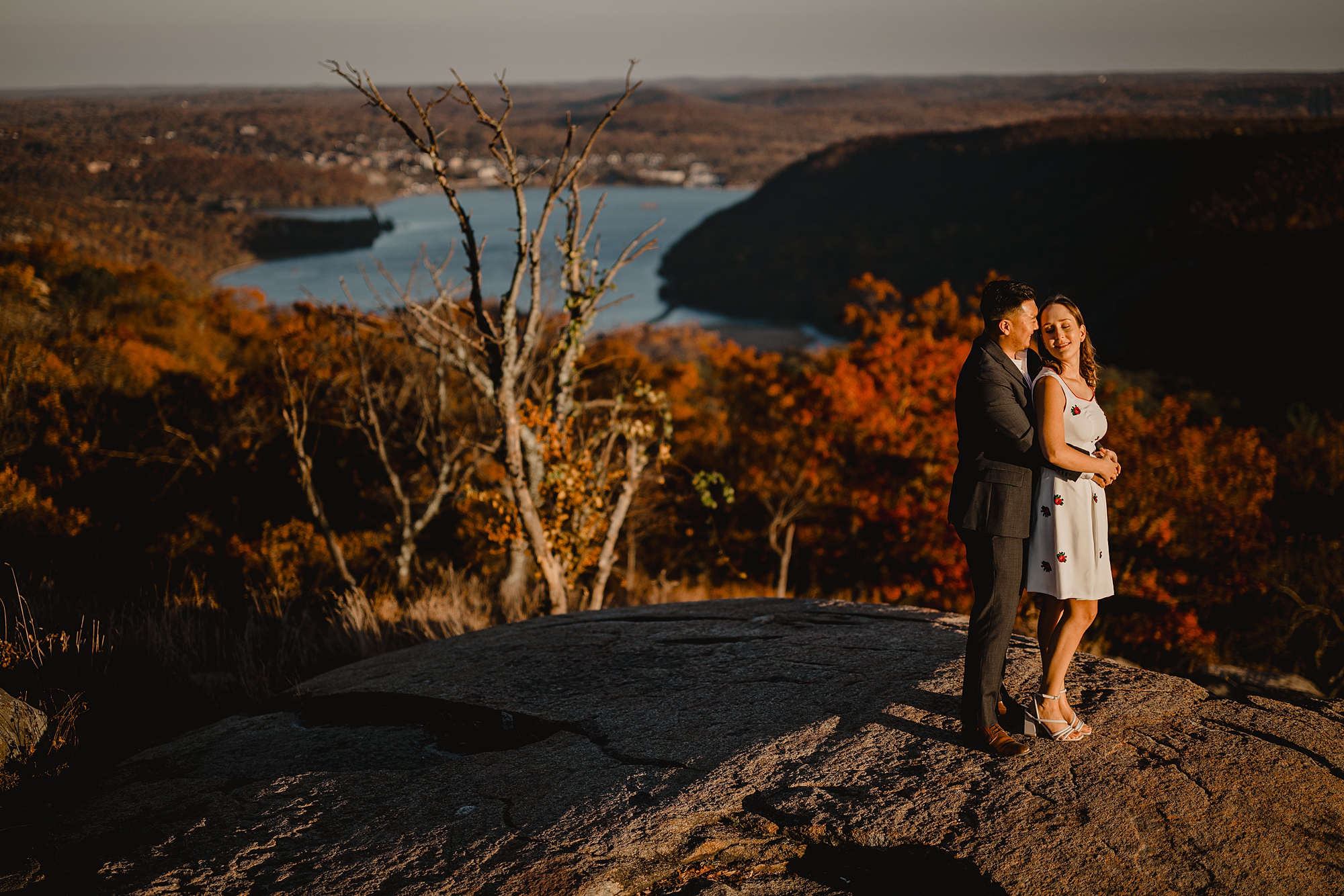 couple hugs in front of red trees during fall engagement session on Bear Mountain
