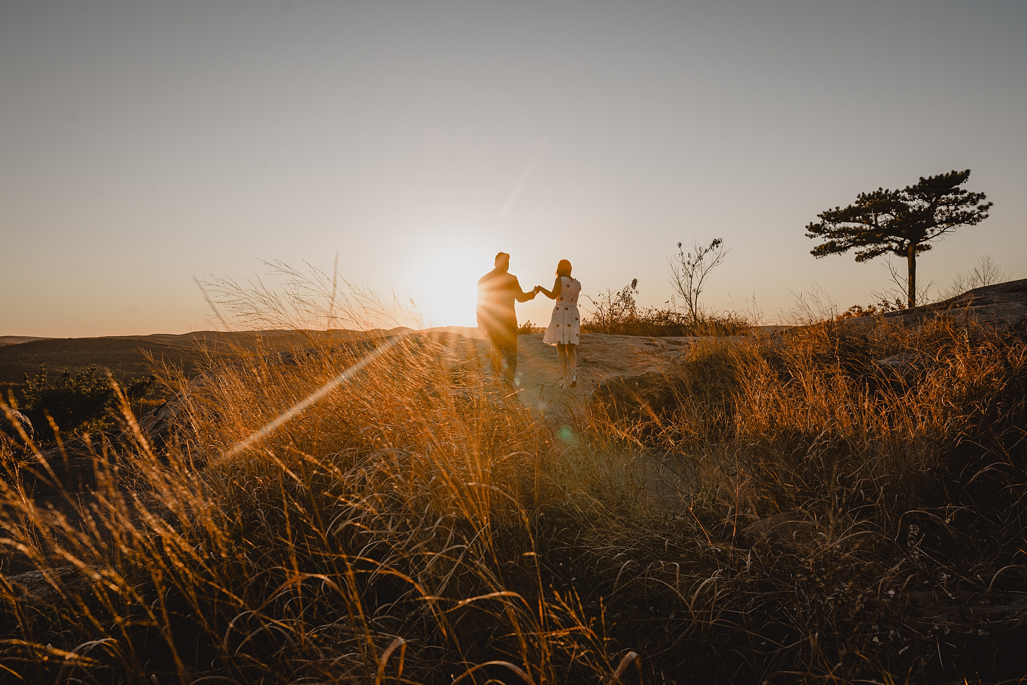 couple stands on top of mountain at sunset during fall engagement session on Bear Mountain