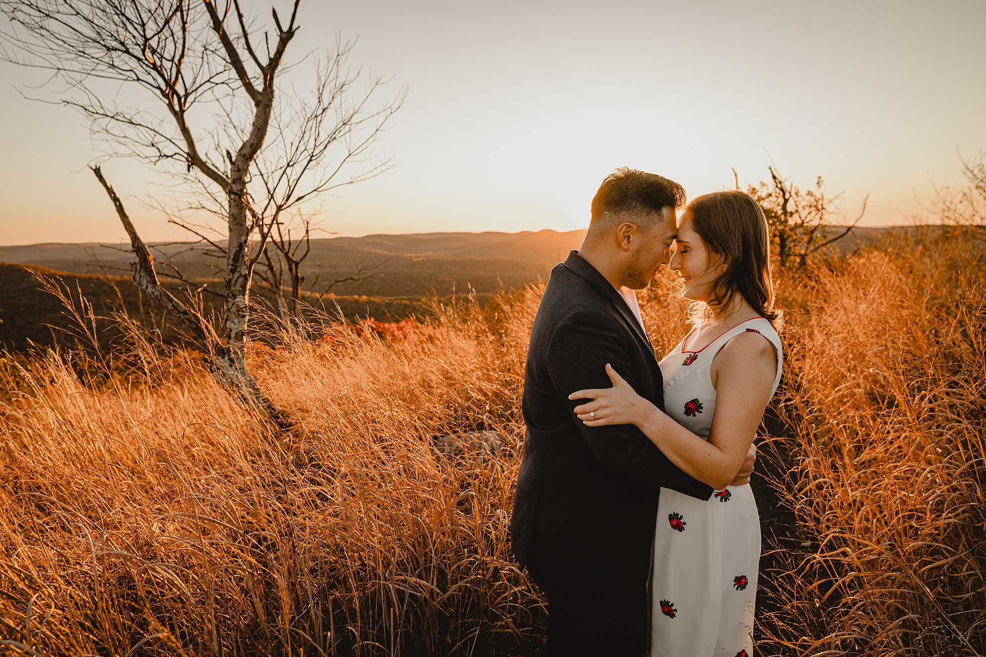 couple stands on top of mountain at sunset during fall engagement session on Bear Mountain