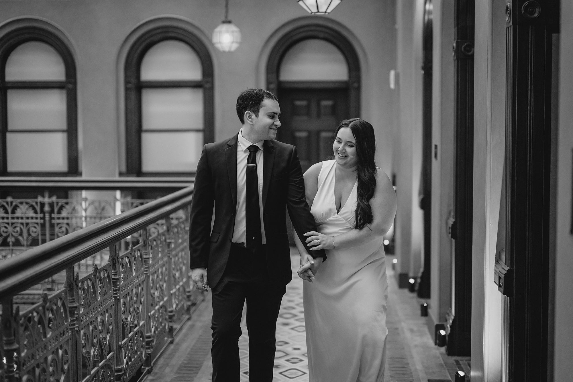 man and woman hold hands walking along balcony during their Beekman Hotel engagement portraits