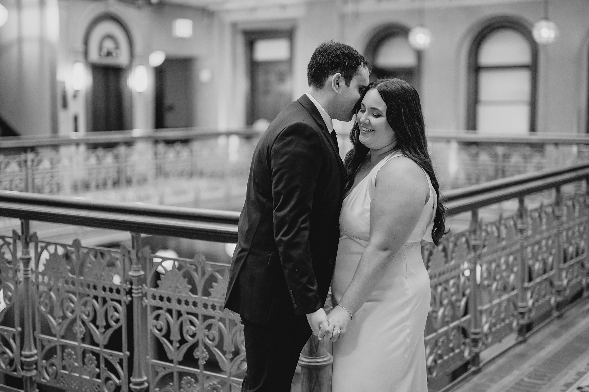 man leans to kiss woman's cheek inside atrium of the Beekman Hotel during engagement portaits