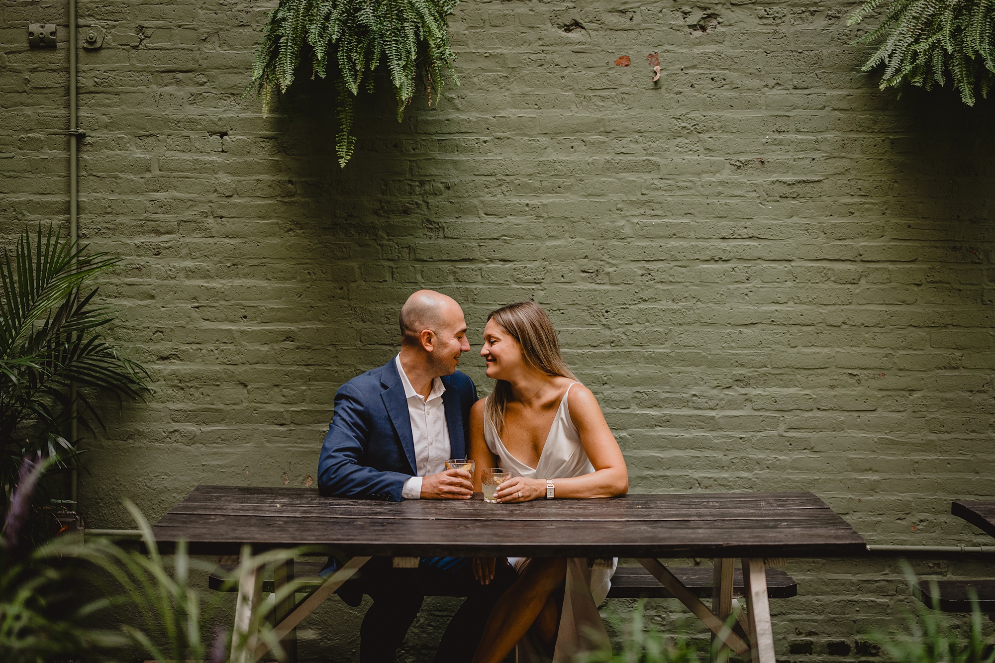 engaged couple hugs in front of green wall at Sundays Well 
