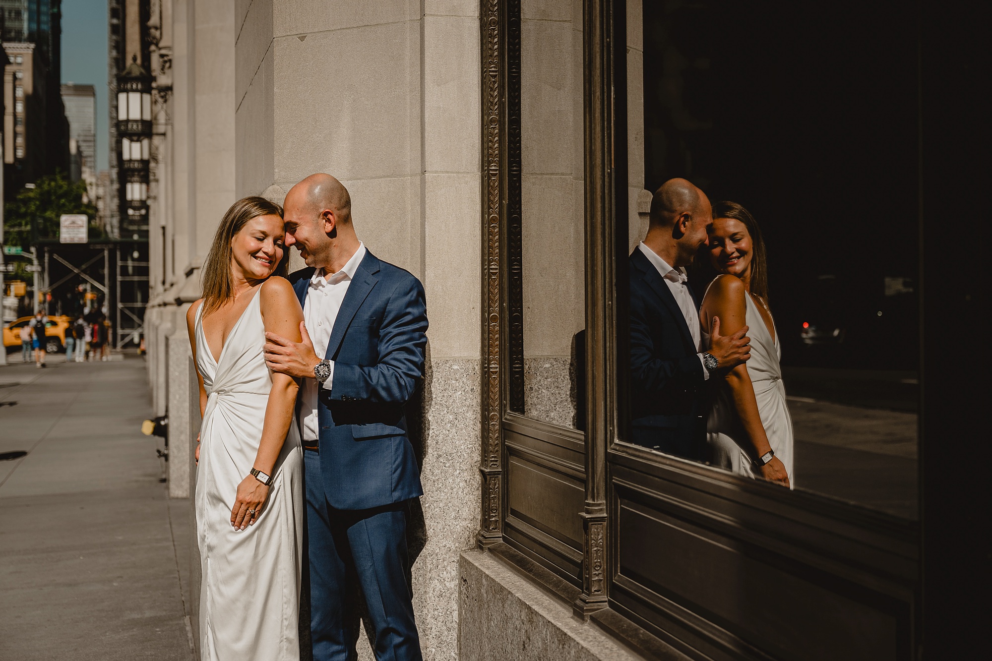 man hugs woman in front of storefront during Murray Hill engagement session