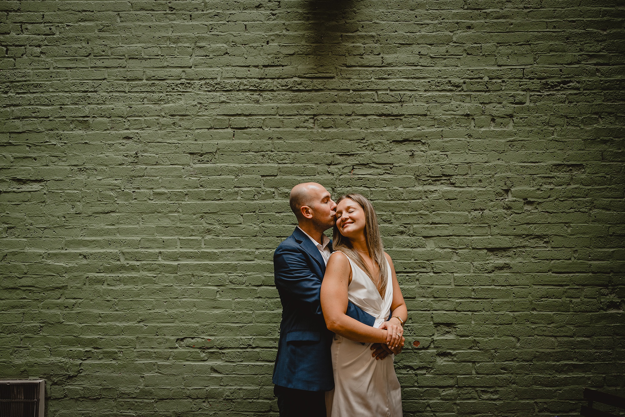 man hugs woman from behind in front of green wall during Murray Hill engagement session