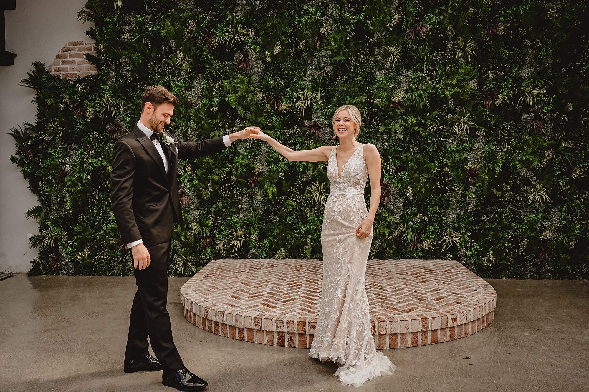 groom looks at bride in front of brick dais at the Refinery at Perona Farms
