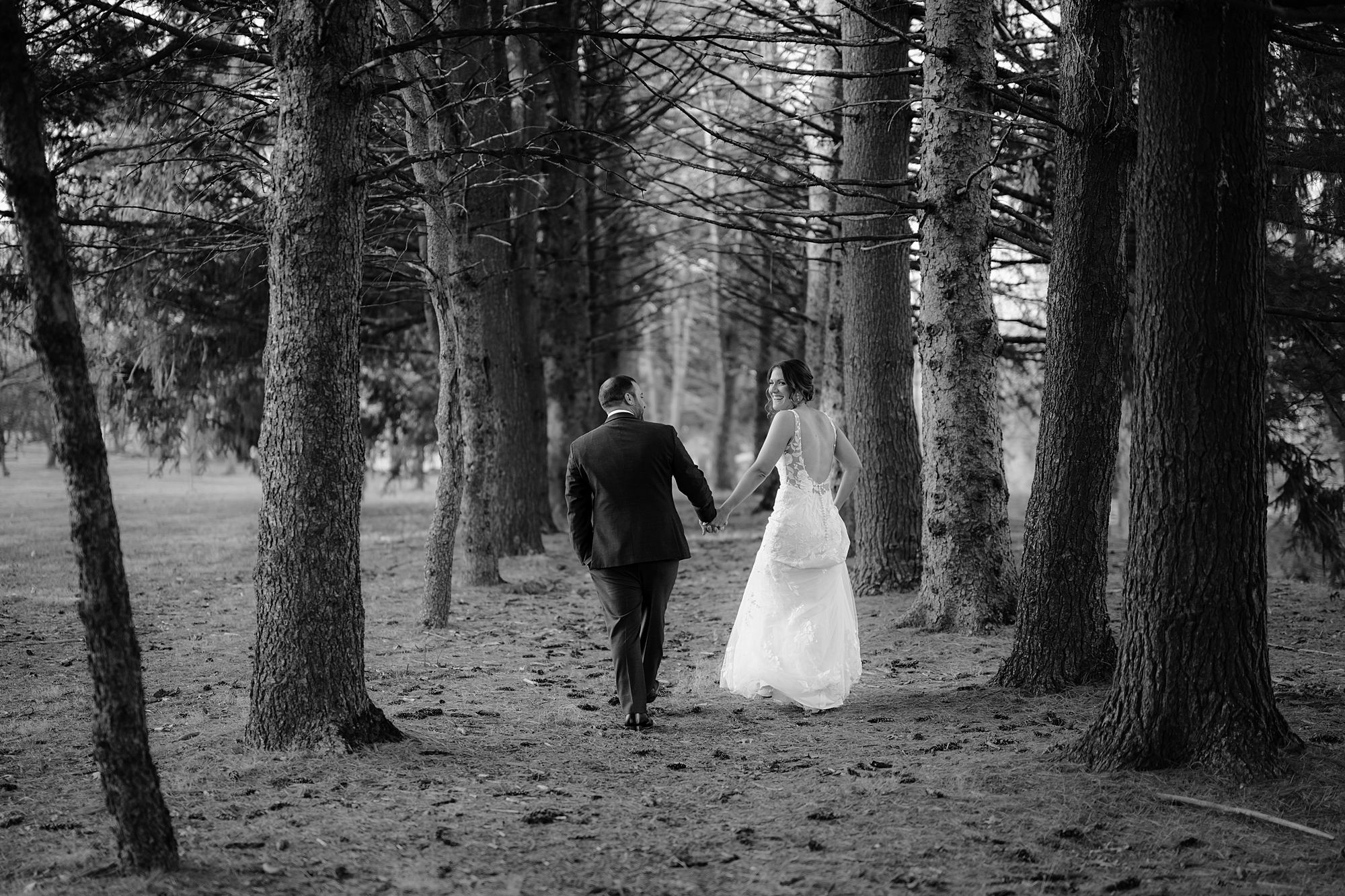 newlyweds hold hands walking through woods at the Refinery at Perona Farms