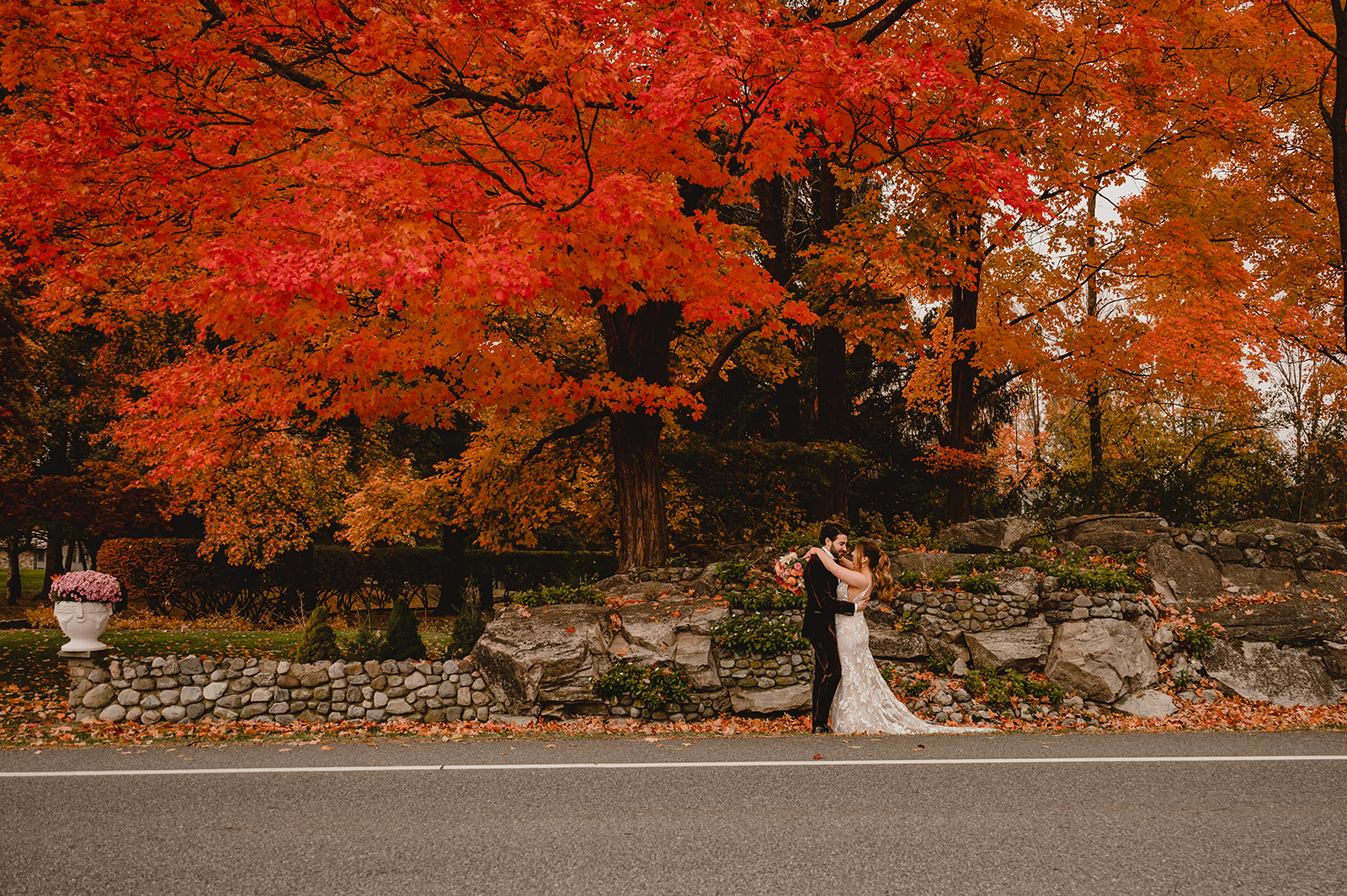 bride and groom hug under red and orange trees outside the Barn at Perona Farms