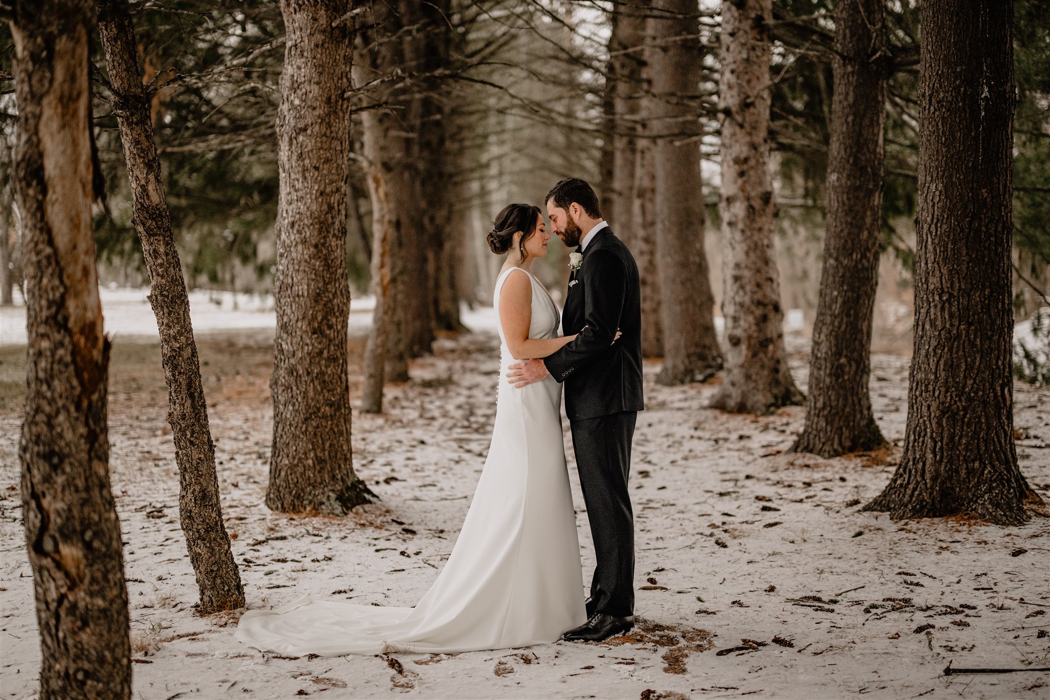 married couple stands between trees in woods in New Jersey 