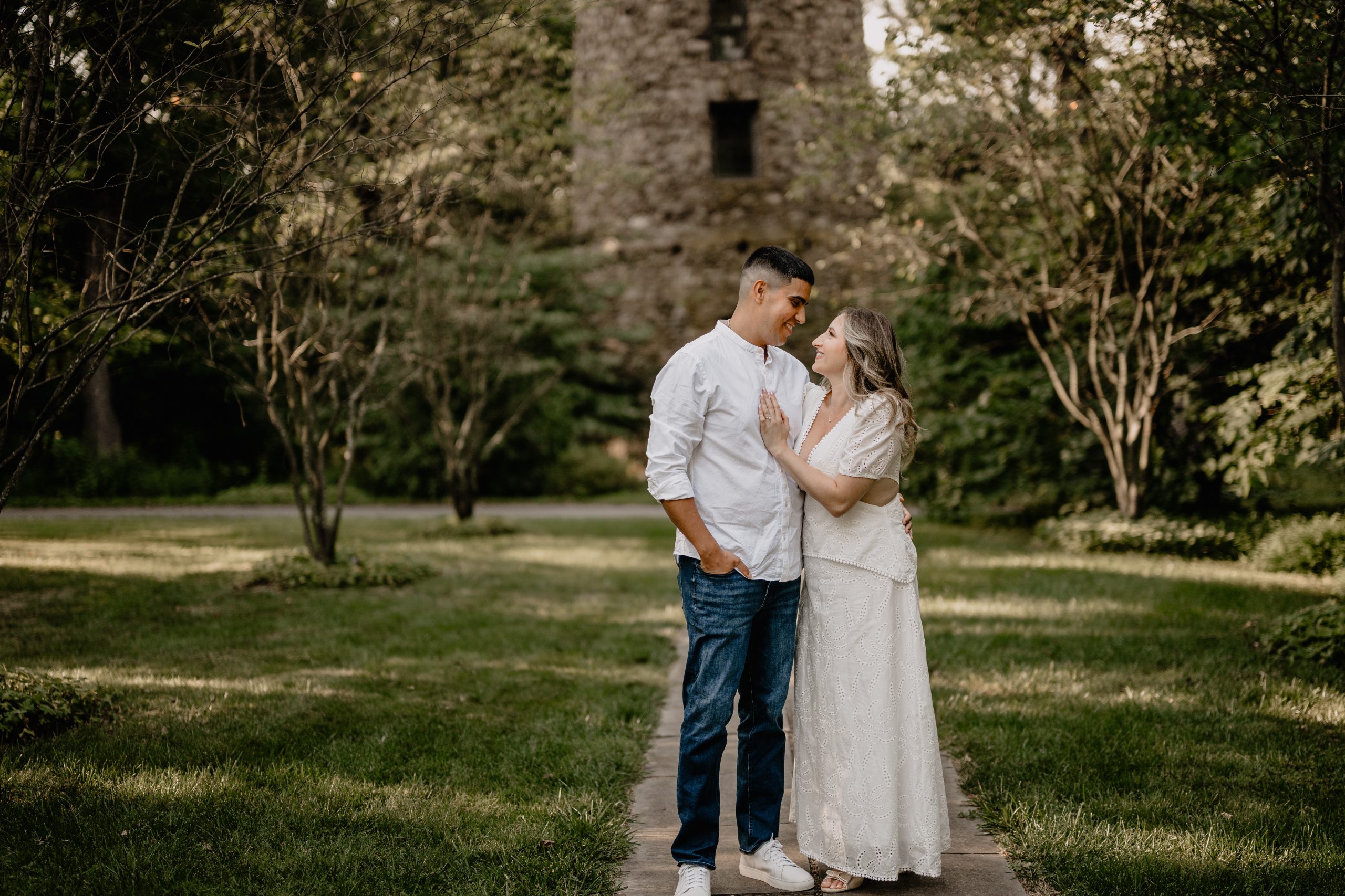 Jaime and Chris standing on the garden path with the stone tower behind them during their Cross Estate Gardens engagement.