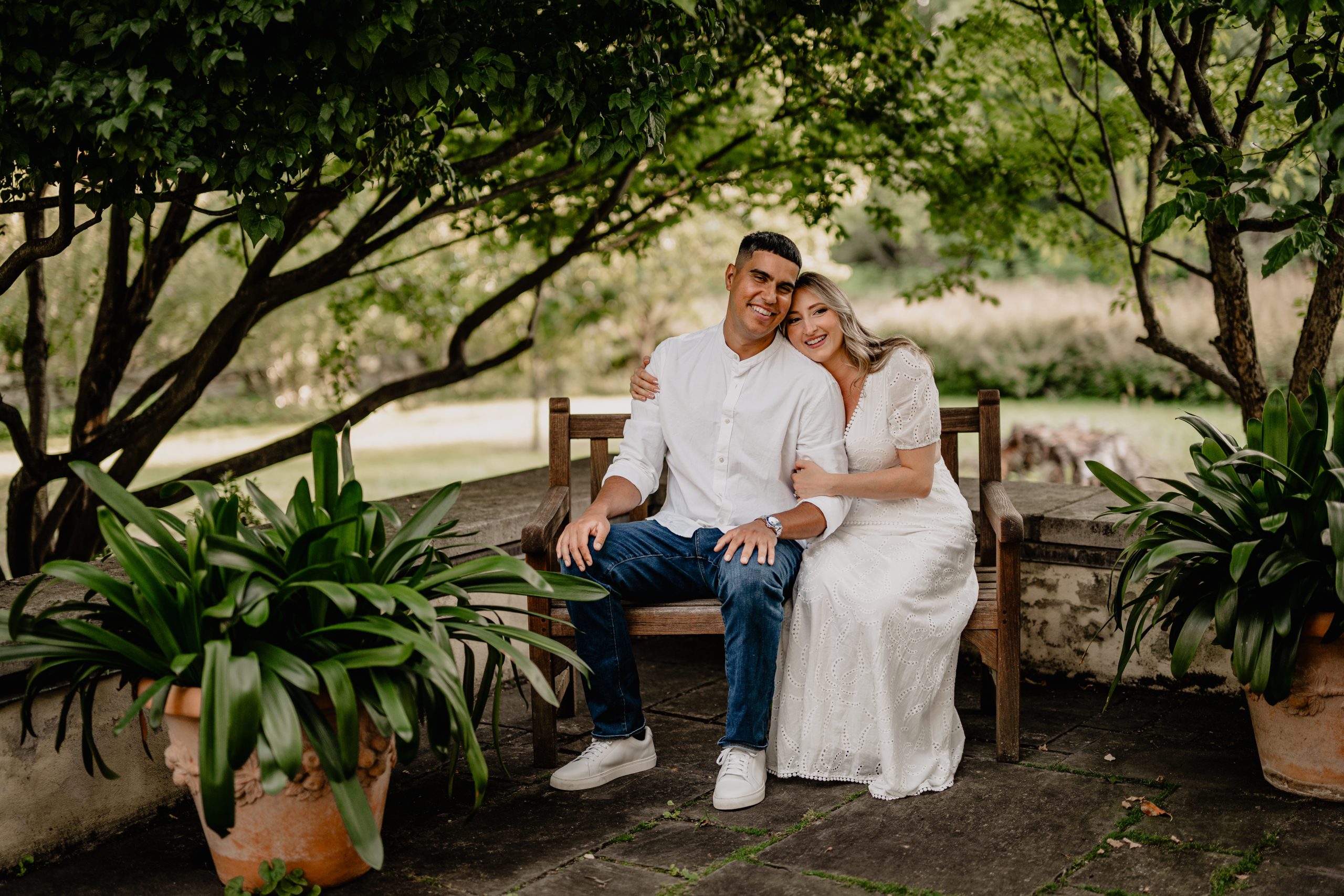 Couple relaxing on a garden bench under the trees during their Cross Estate Gardens engagement.