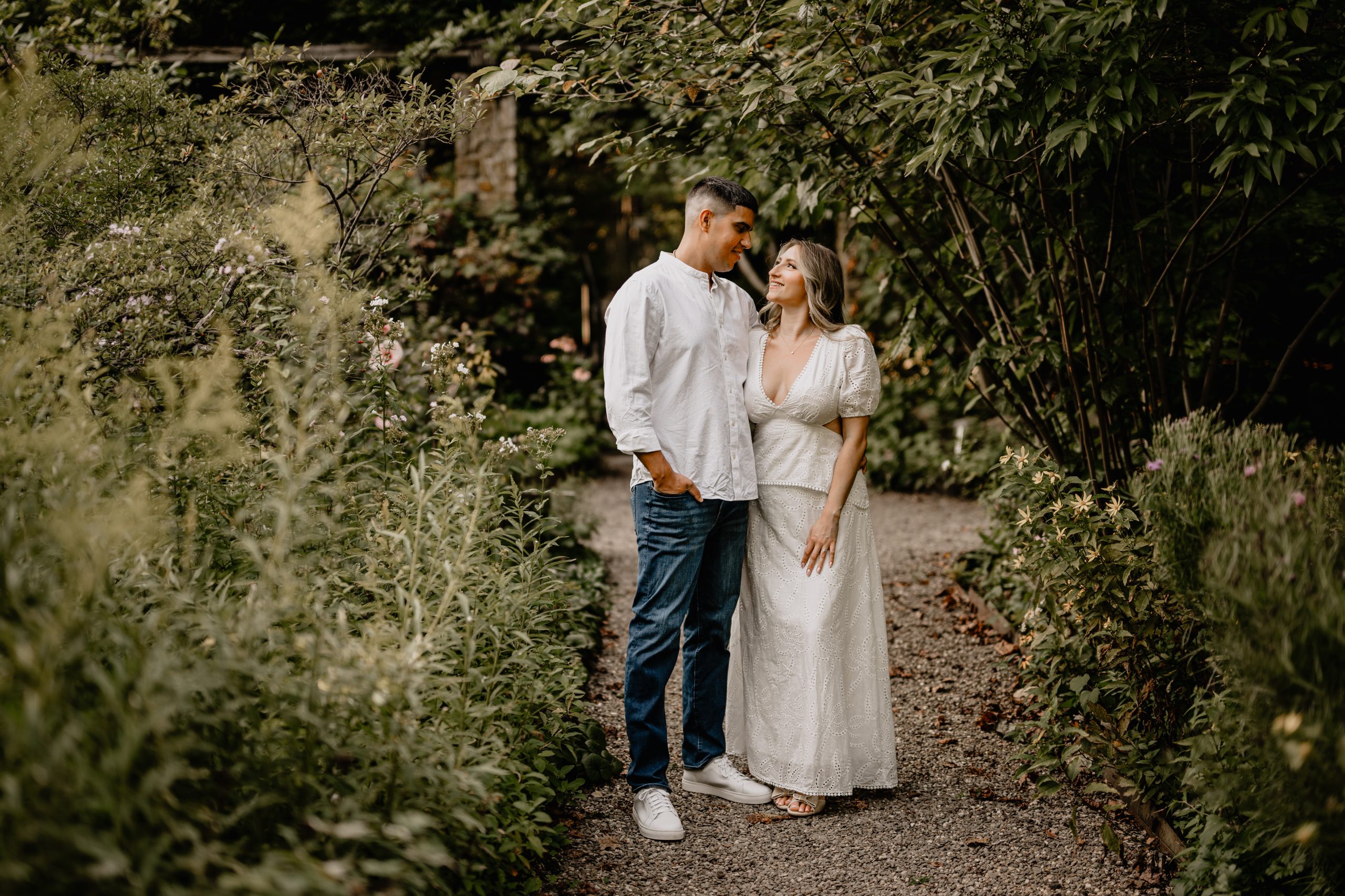 Jaime and Chris standing together on a flower-lined path during their Cross Estate Gardens engagement.