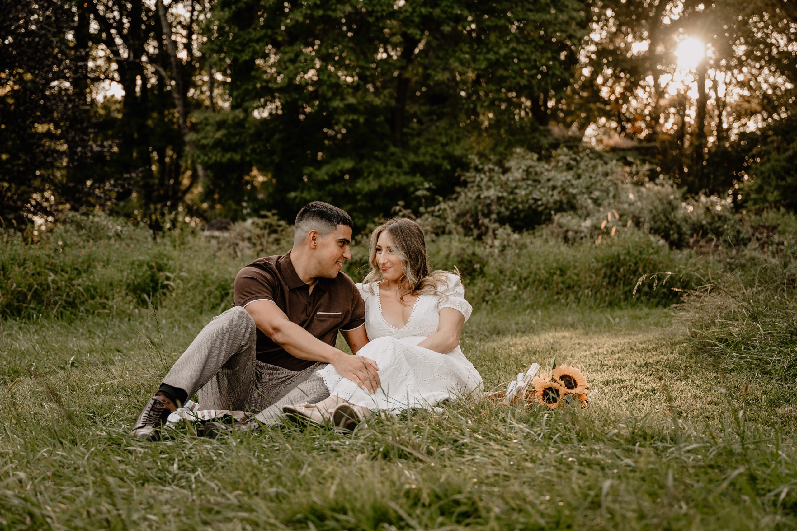Couple having a picnic in the grass with sunflowers during their Cross Estate Gardens engagement.