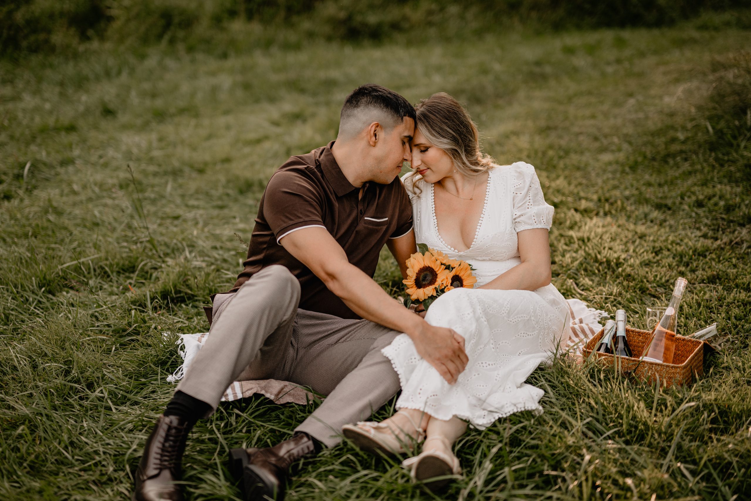 Couple having a picnic in the grass with sunflowers during their Cross Estate Gardens engagement.