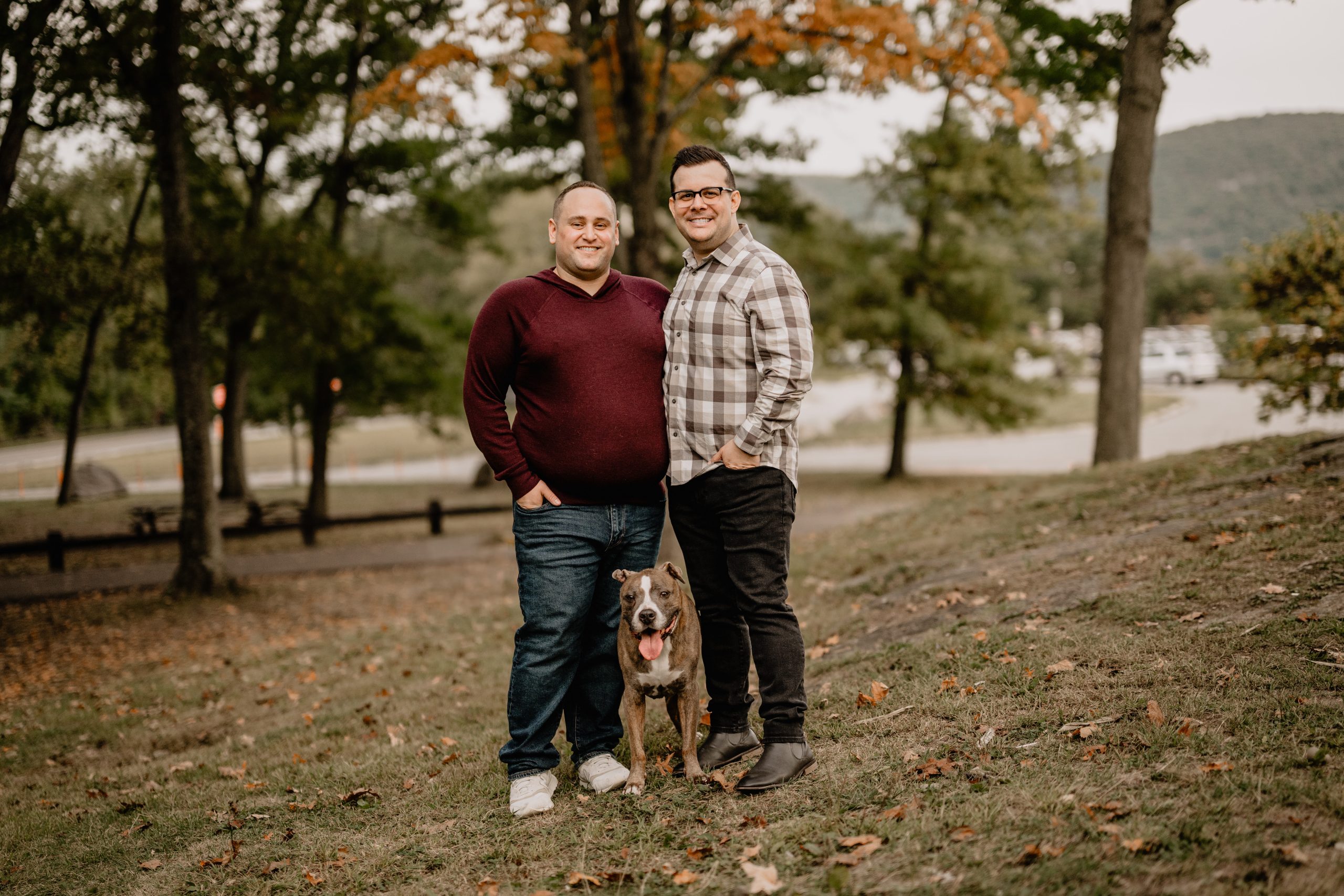 Trevor and Josh standing together with their dog Duke during their Bear Mountain engagement.