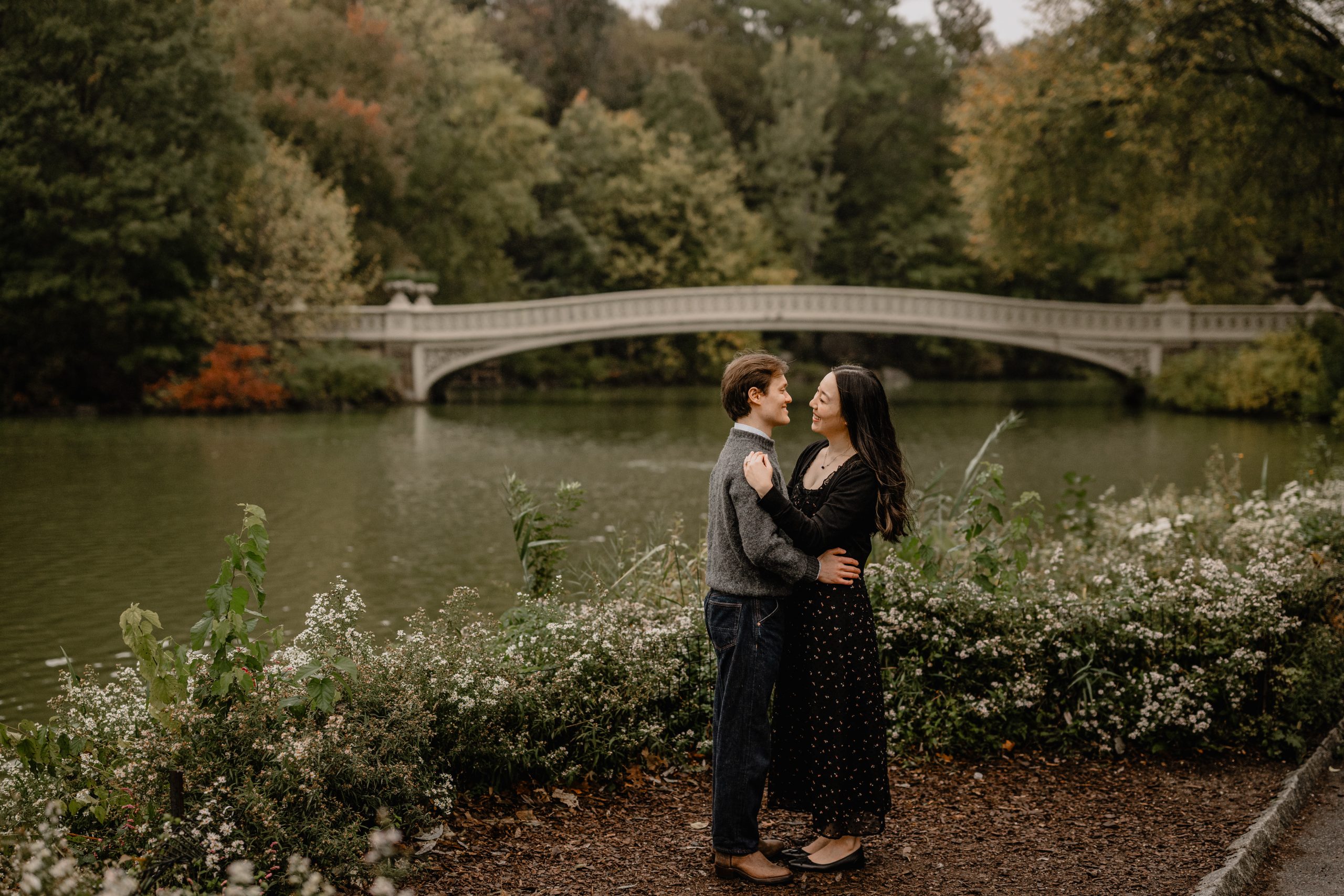 Kimberly and Peter sharing a sweet moment by the water during their fall engagement session at Central Park with the Bow Bridge in the background.