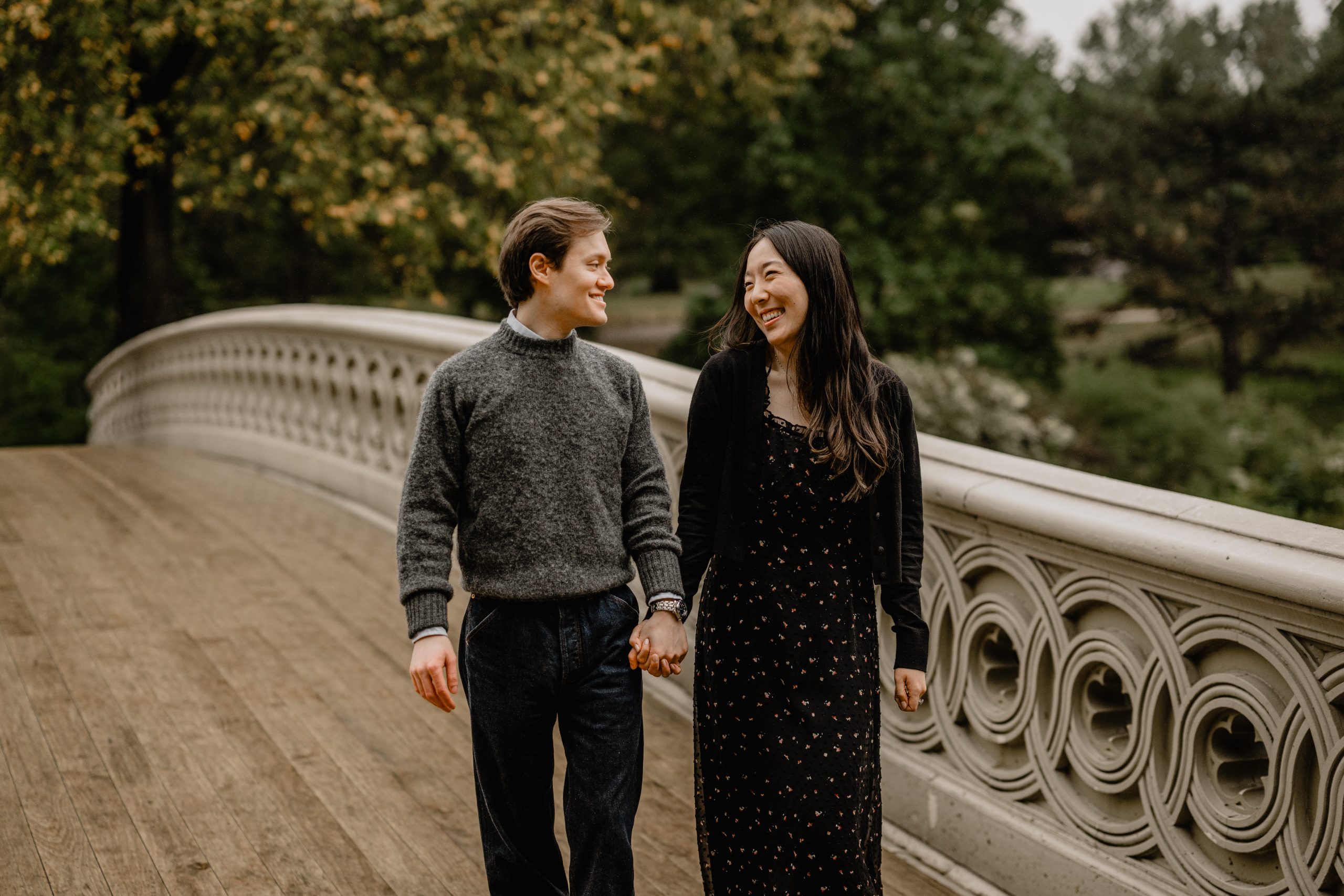 Kimberly and Peter standing on the Bow Bridge during their fall engagement session at Central Park, smiling at each other.