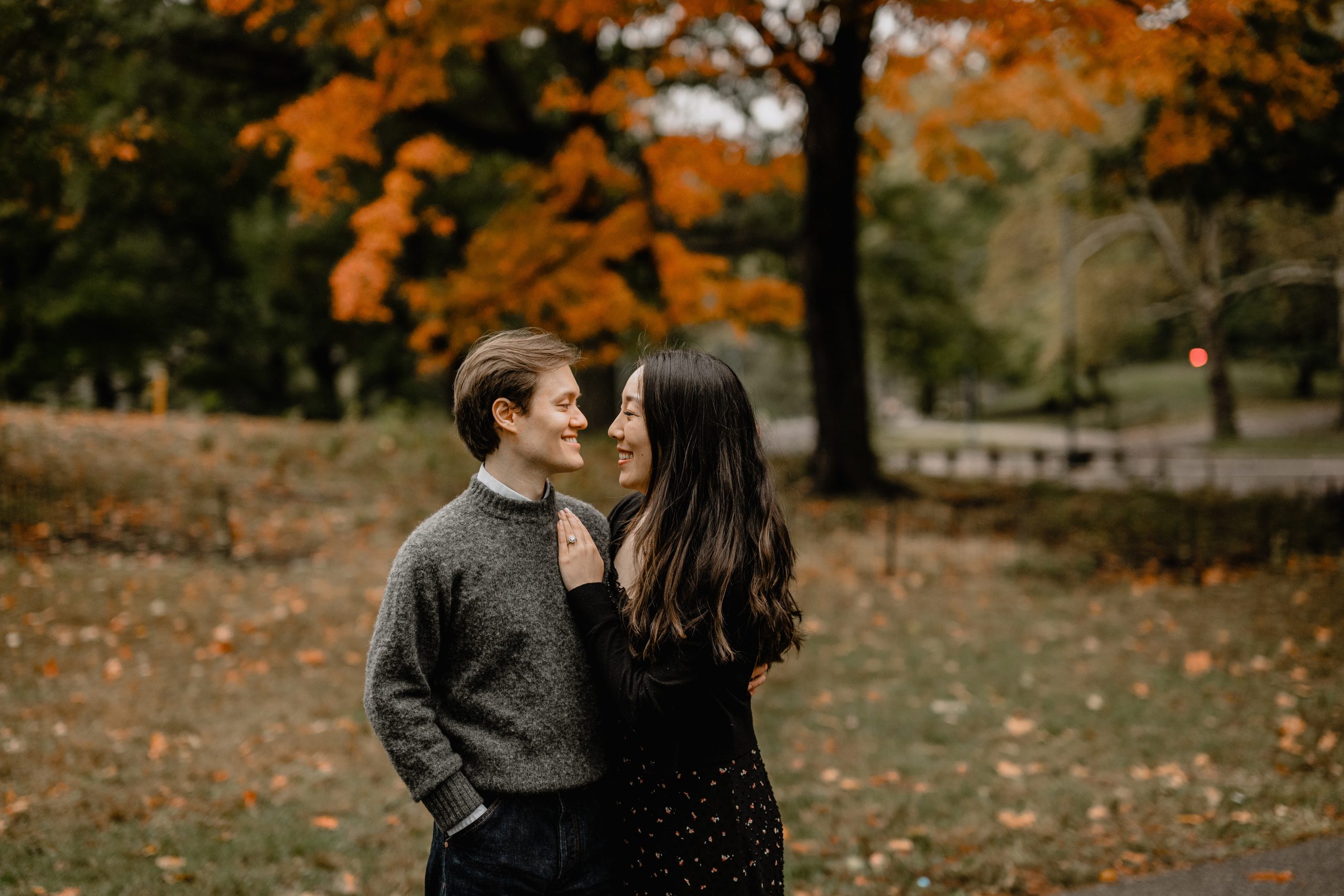 Kimberly and Peter holding hands and smiling at each other during their fall engagement session at Central Park, surrounded by fall foliage.