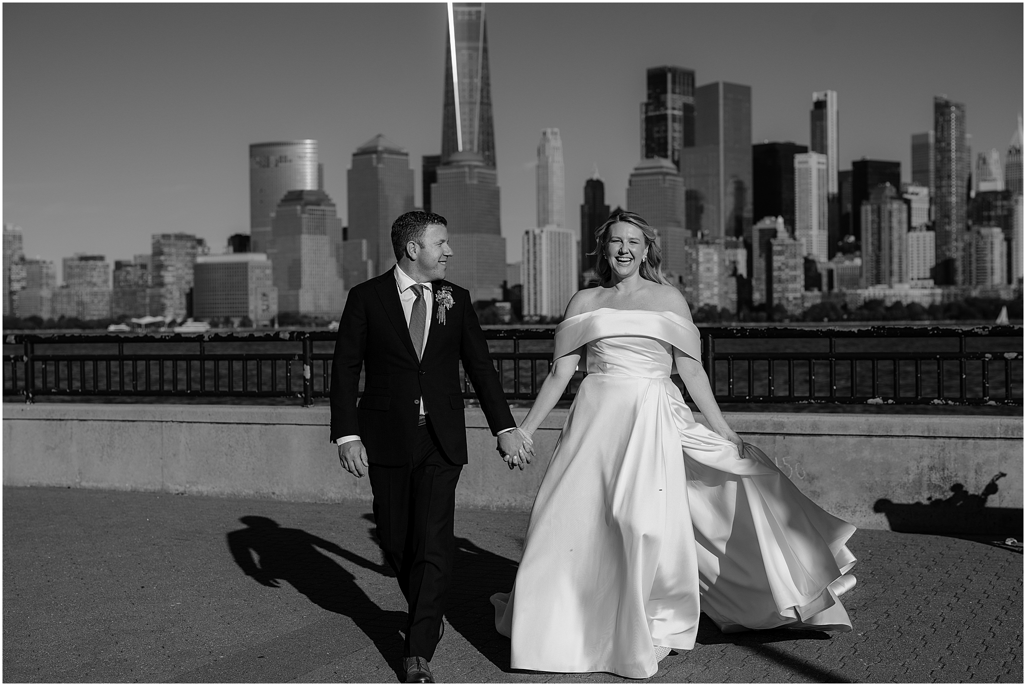 Couple walking hand-in-hand, smiling with the stunning NYC skyline as the backdrop at their Colorful Fall Wedding at Liberty House.