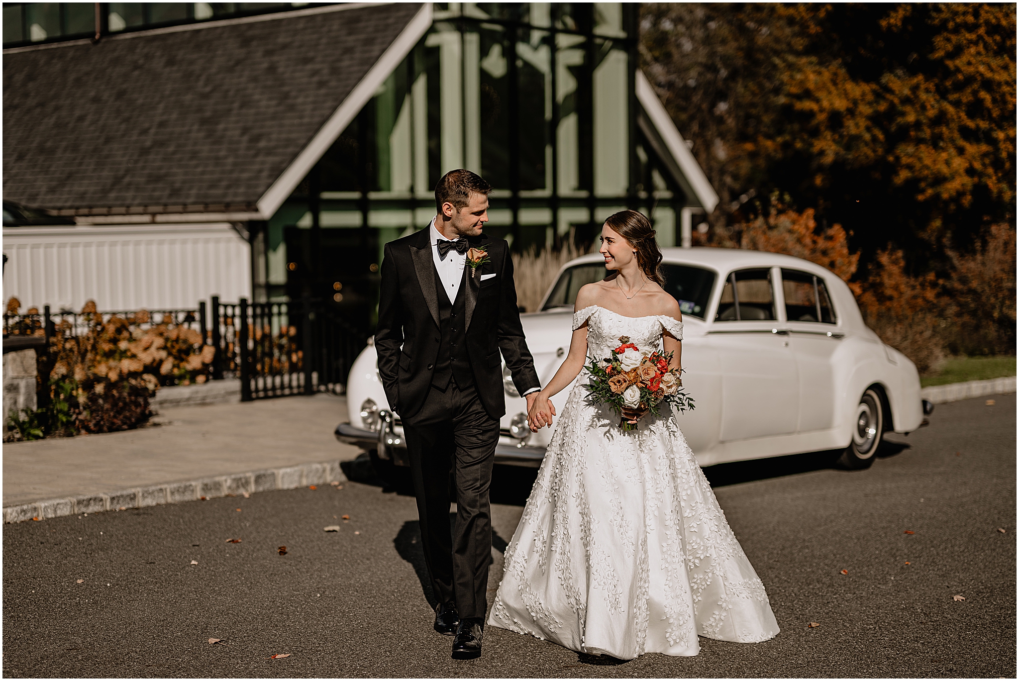 Couple walking hand-in-hand with the vintage car behind them before their fall wedding at Crossed Keys Estate.