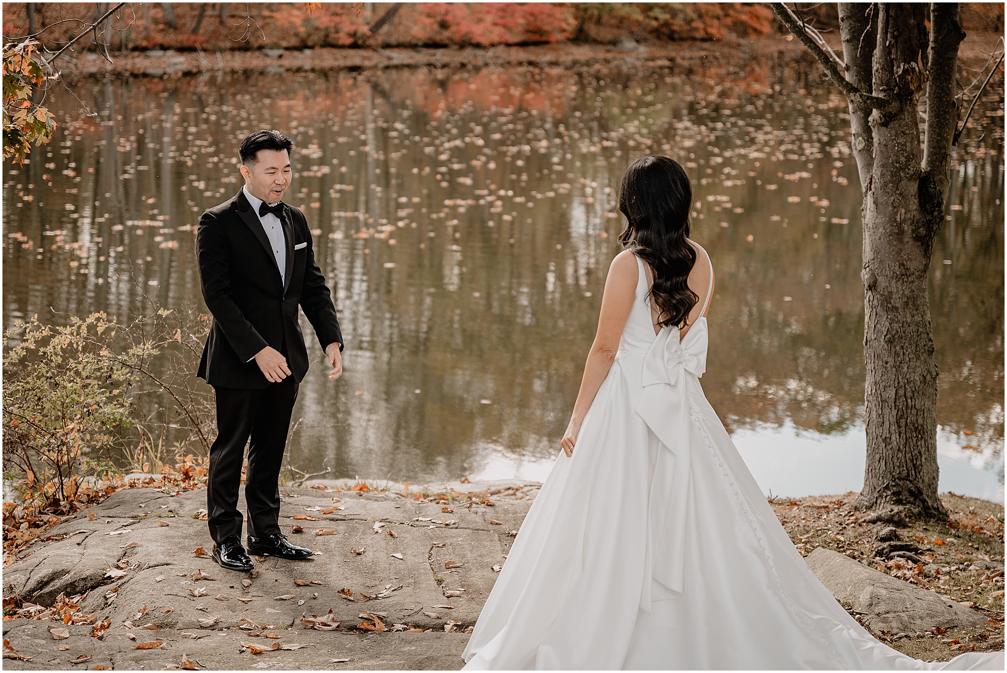 Couple's first look by the lake before their fall wedding at Perona Farms Reserve, surrounded by vibrant fall foliage, creating a romantic and unforgettable moment.