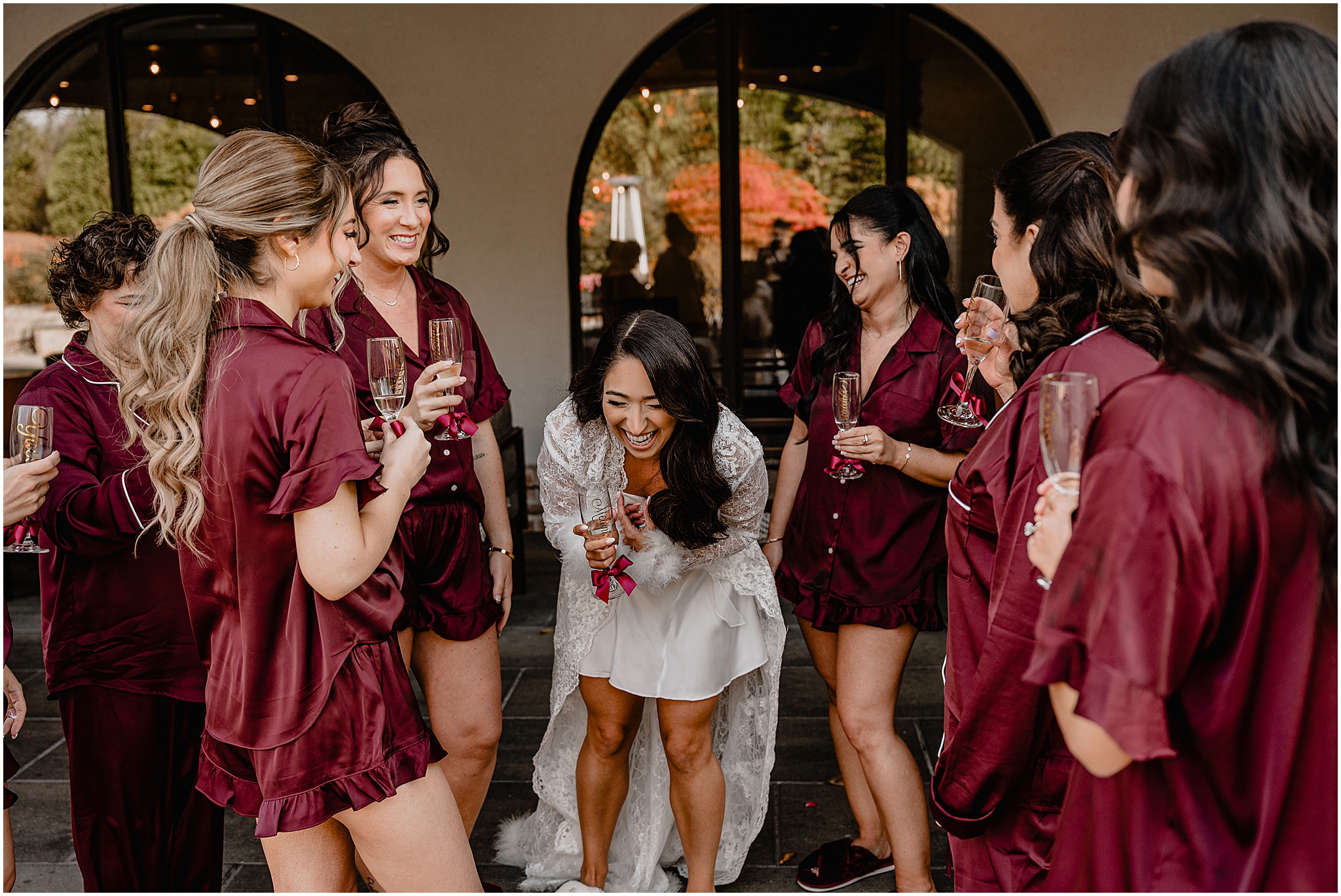 Bride laughing and drinking champagne with her bridesmaids during her fall wedding at Perona Farms Refinery before the ceremony.