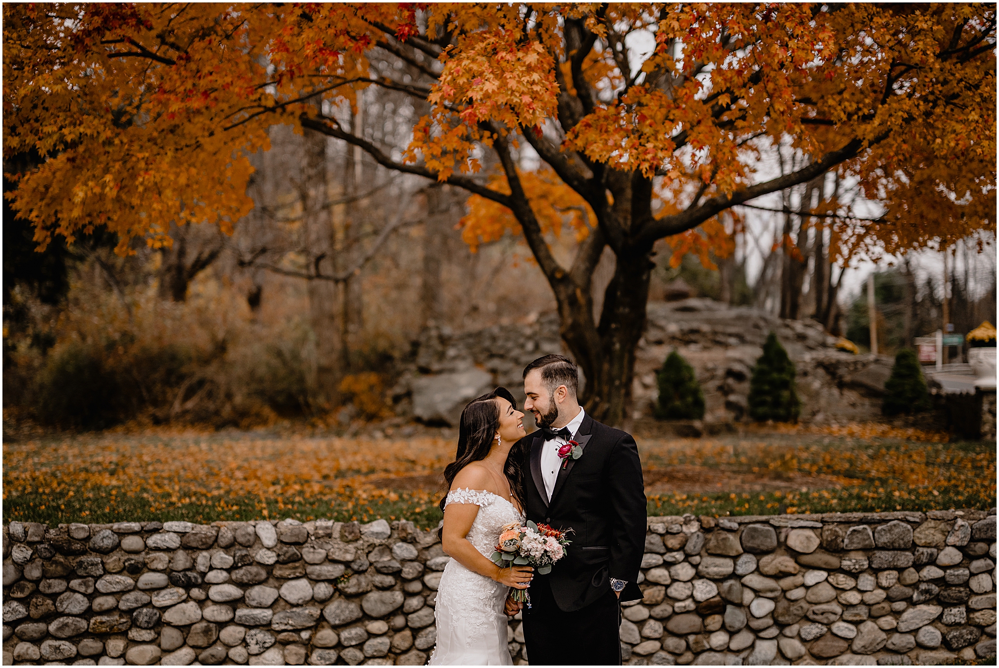 Couple’s stunning portraits in front of a beautiful autumn tree before their fall wedding at Perona Farms Refinery, bathed in soft light and surrounded by vibrant fall foliage.