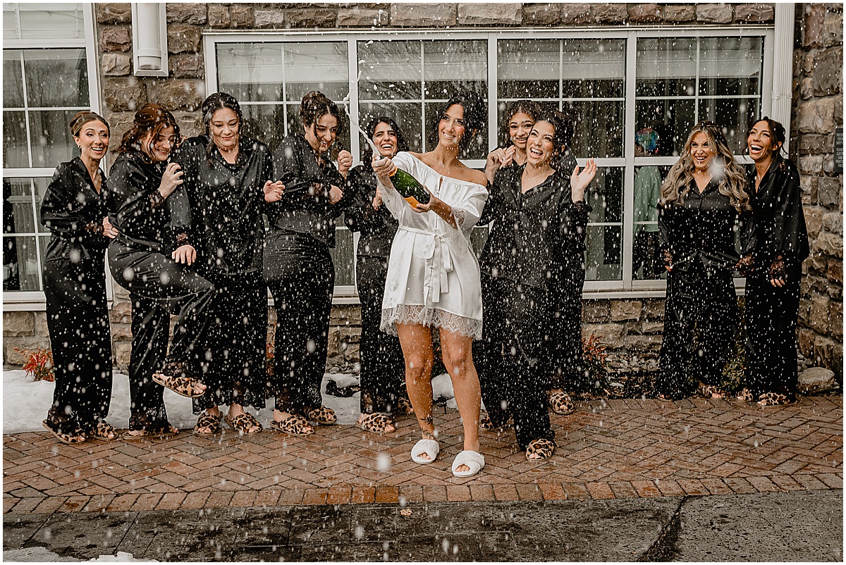 Bride opening a champagne bottle before her winter Hamilton Manor wedding.