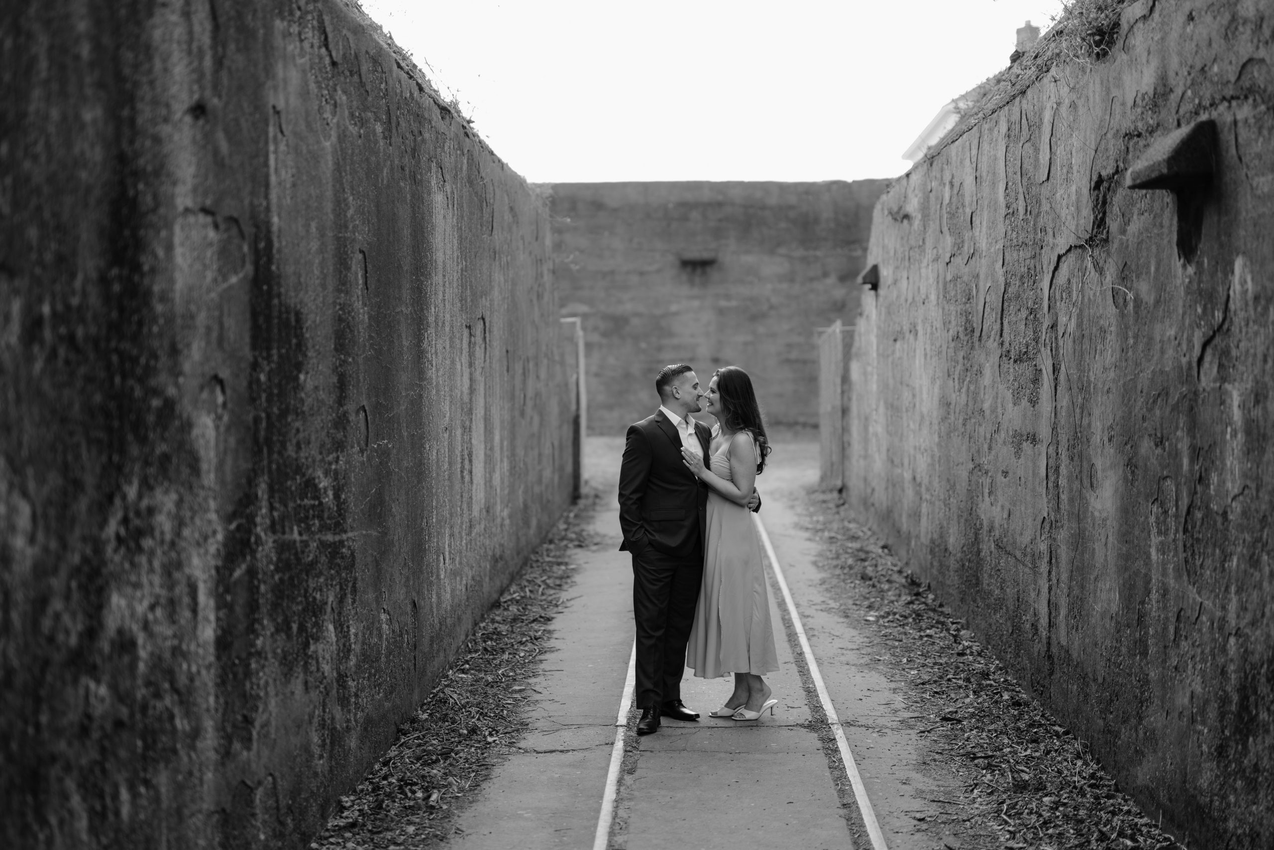 Couple standing in the middle of two big walls on their engagement session at Sandy Hook Beach.